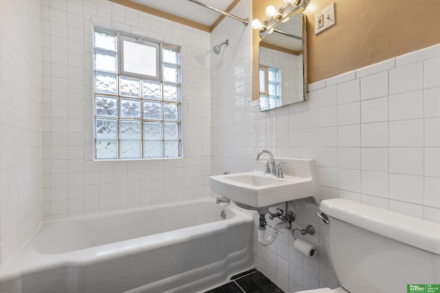 full bath with tile walls, toilet, washtub / shower combination, and a sink