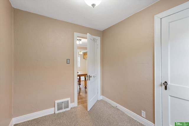 interior space featuring light colored carpet, visible vents, a textured wall, and baseboards