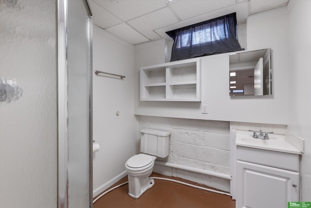 bathroom featuring concrete floors, a drop ceiling, toilet, vanity, and concrete block wall