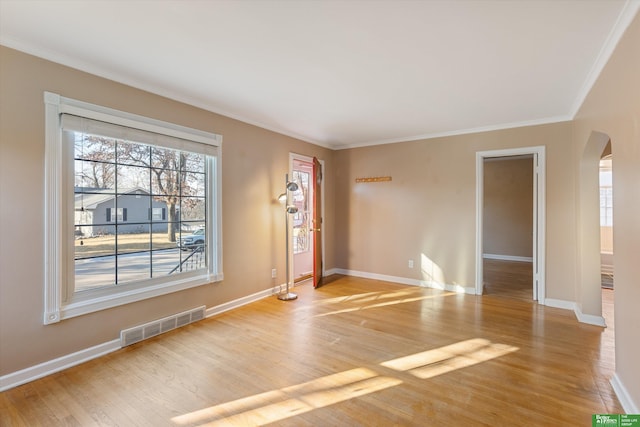 unfurnished room featuring visible vents, light wood finished floors, baseboards, arched walkways, and crown molding