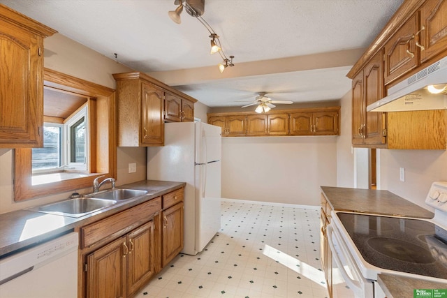 kitchen featuring white appliances, brown cabinetry, light floors, a sink, and under cabinet range hood