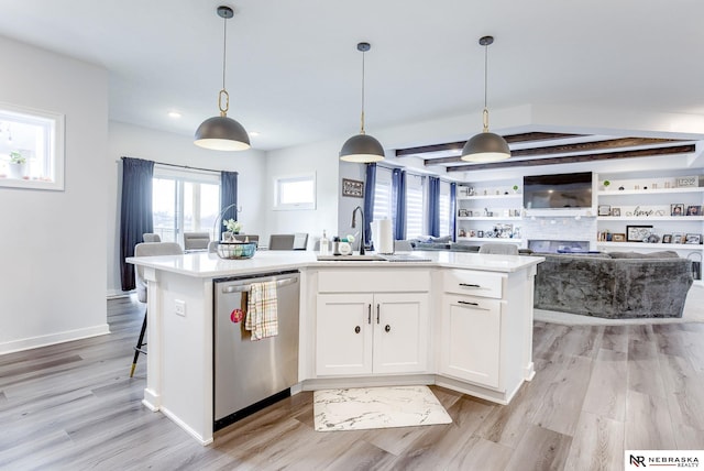 kitchen with a center island with sink, stainless steel dishwasher, white cabinetry, light wood-style floors, and light countertops