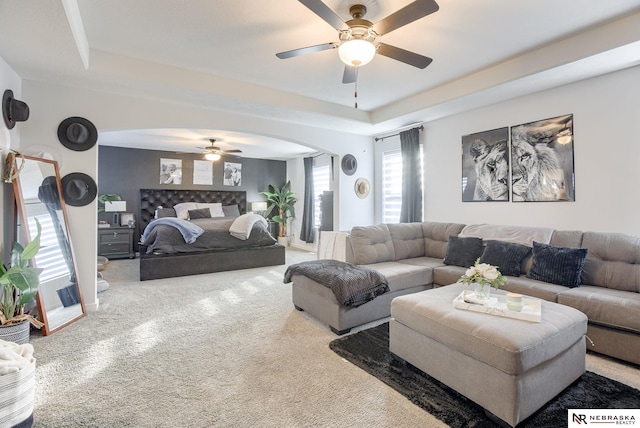 carpeted living area featuring arched walkways, a tray ceiling, and a ceiling fan