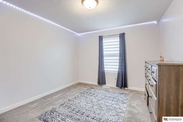 interior space featuring light carpet, a textured ceiling, and baseboards