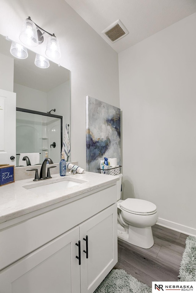 bathroom with vanity, wood finished floors, visible vents, toilet, and a shower with door