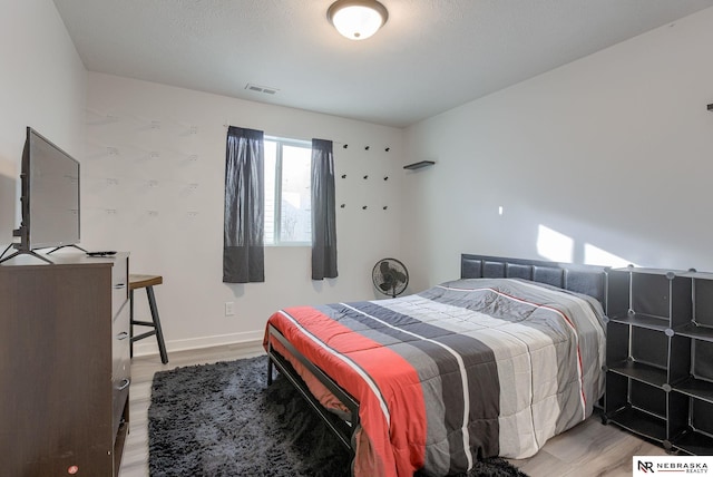 bedroom featuring light wood finished floors, visible vents, and baseboards