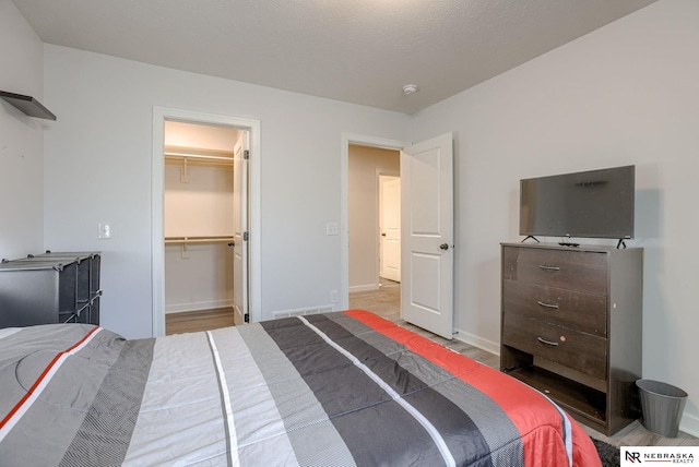 bedroom featuring a closet, a walk in closet, baseboards, and wood finished floors