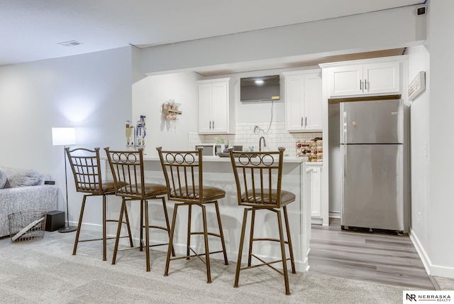 kitchen featuring visible vents, freestanding refrigerator, white cabinetry, a kitchen breakfast bar, and tasteful backsplash