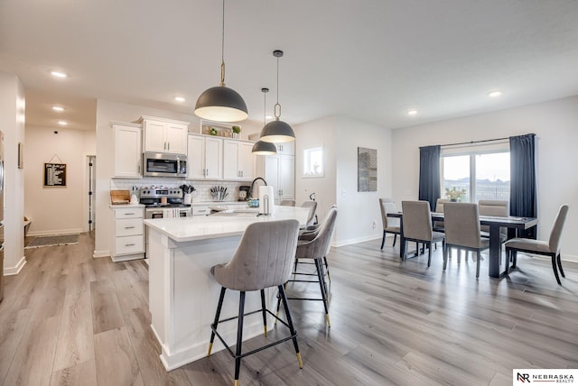 kitchen with a sink, white cabinetry, stainless steel appliances, a breakfast bar area, and decorative backsplash