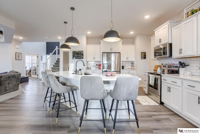 kitchen featuring a kitchen bar, light countertops, appliances with stainless steel finishes, white cabinetry, and a sink