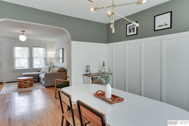 dining space with a wainscoted wall, light wood finished floors, arched walkways, a decorative wall, and a notable chandelier