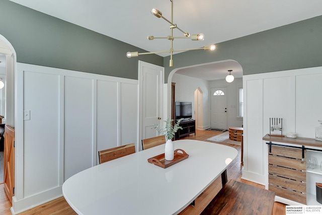 dining area featuring light wood-type flooring, arched walkways, a wainscoted wall, and a decorative wall