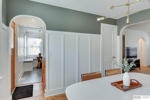 dining room with light wood-type flooring, arched walkways, wainscoting, and a decorative wall