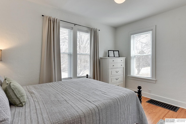 bedroom with multiple windows, wood finished floors, visible vents, and baseboards