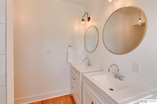 bathroom featuring wood finished floors, two vanities, baseboards, and a sink