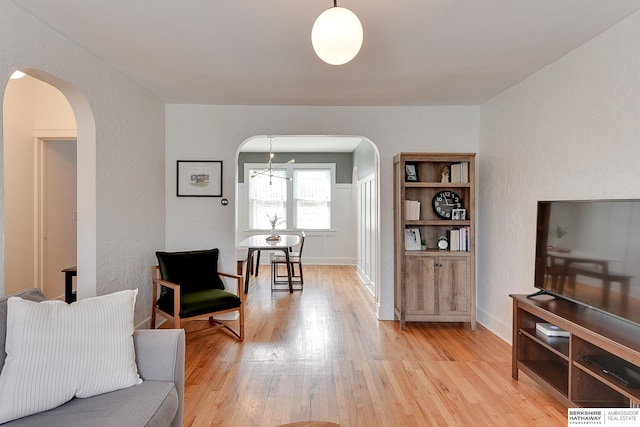 living area featuring arched walkways, light wood-style flooring, and baseboards