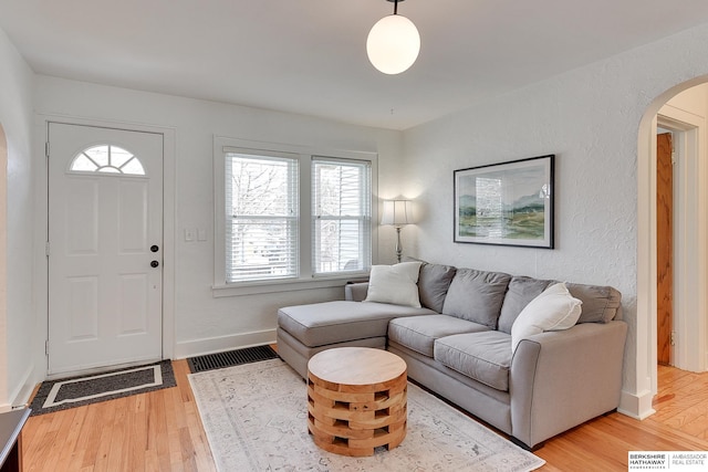 living area featuring baseboards, arched walkways, and light wood finished floors