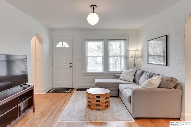 living room with arched walkways, light wood-type flooring, and baseboards