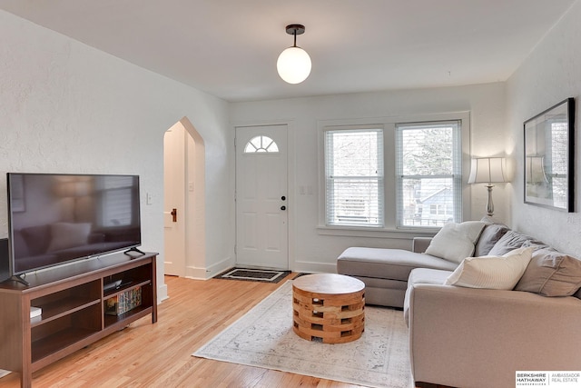 living area featuring baseboards, arched walkways, and light wood finished floors