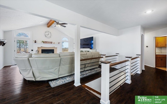 living area featuring a glass covered fireplace, vaulted ceiling with beams, a ceiling fan, and wood-type flooring