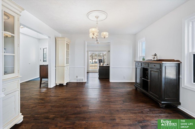 unfurnished dining area featuring baseboards, wood finished floors, visible vents, and a chandelier