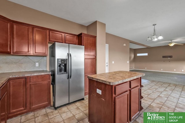 kitchen featuring backsplash, a center island, stainless steel fridge with ice dispenser, ceiling fan with notable chandelier, and hanging light fixtures