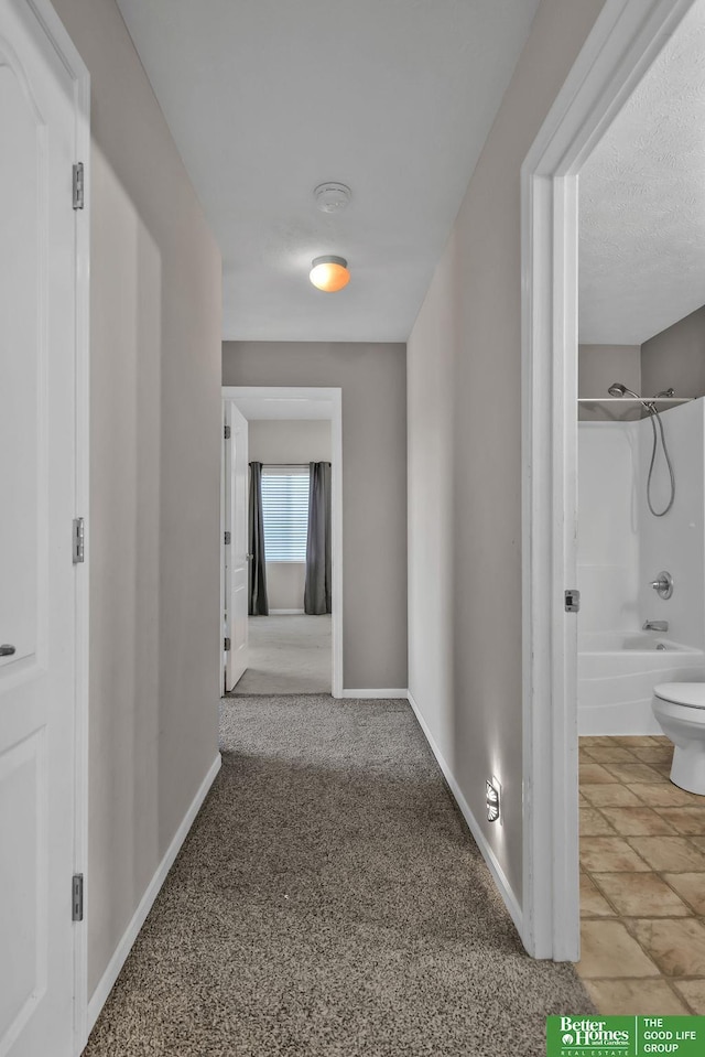 hall with baseboards, carpet, and a textured ceiling