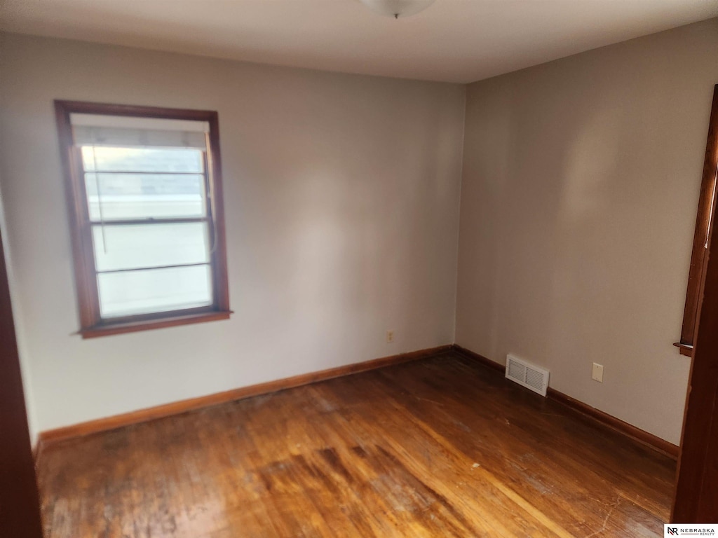 empty room with dark wood-style floors, visible vents, and baseboards