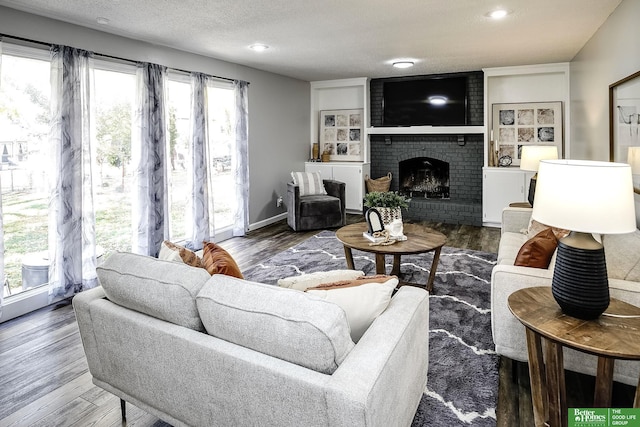 living room featuring a fireplace, wood finished floors, baseboards, and a textured ceiling