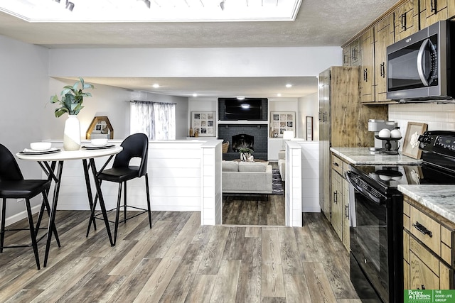 kitchen with wood finished floors, decorative backsplash, black range with electric cooktop, a textured ceiling, and stainless steel microwave