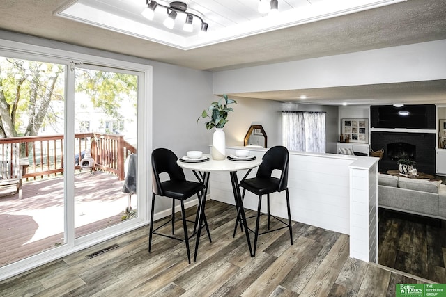 dining area with visible vents, a brick fireplace, wood finished floors, a textured ceiling, and a raised ceiling