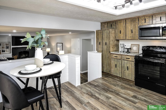 kitchen featuring stainless steel microwave, backsplash, black range with electric stovetop, brown cabinets, and dark wood-style floors