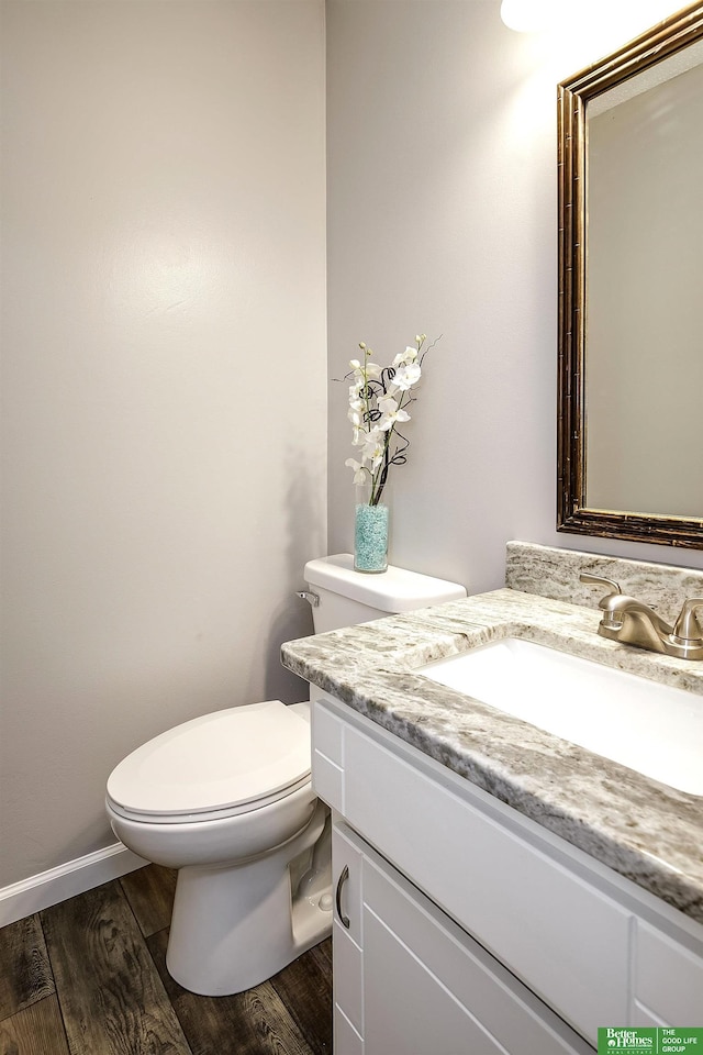 half bathroom with vanity, toilet, wood finished floors, and baseboards