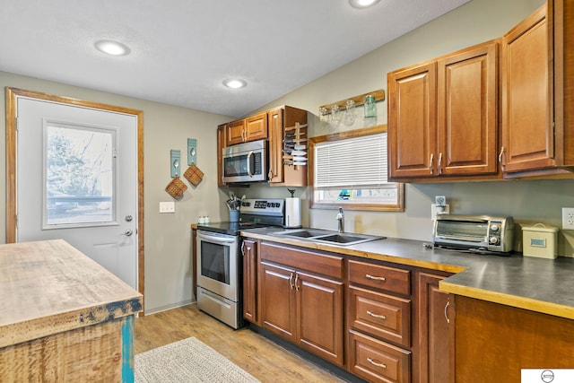 kitchen with a toaster, appliances with stainless steel finishes, light wood-style floors, brown cabinetry, and a sink