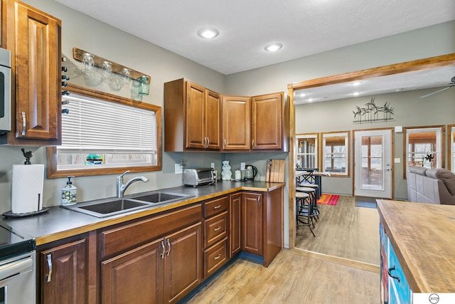 kitchen with butcher block countertops, a ceiling fan, a sink, open floor plan, and light wood-style floors