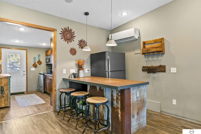 kitchen featuring wood finished floors, butcher block countertops, an AC wall unit, appliances with stainless steel finishes, and a kitchen bar