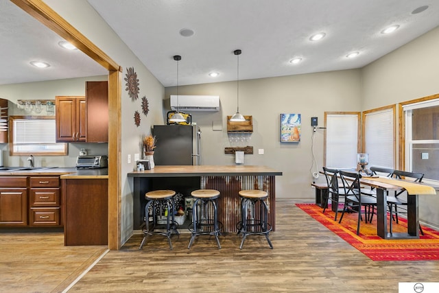 kitchen with light wood finished floors, freestanding refrigerator, a sink, an AC wall unit, and a kitchen breakfast bar