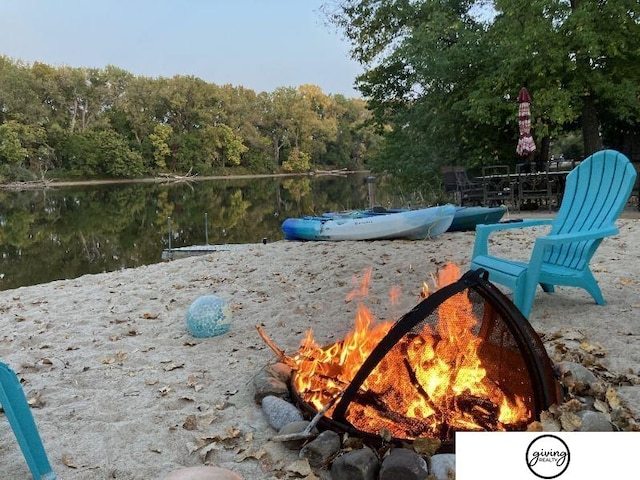 exterior space featuring an outdoor fire pit, a water view, and a view of trees