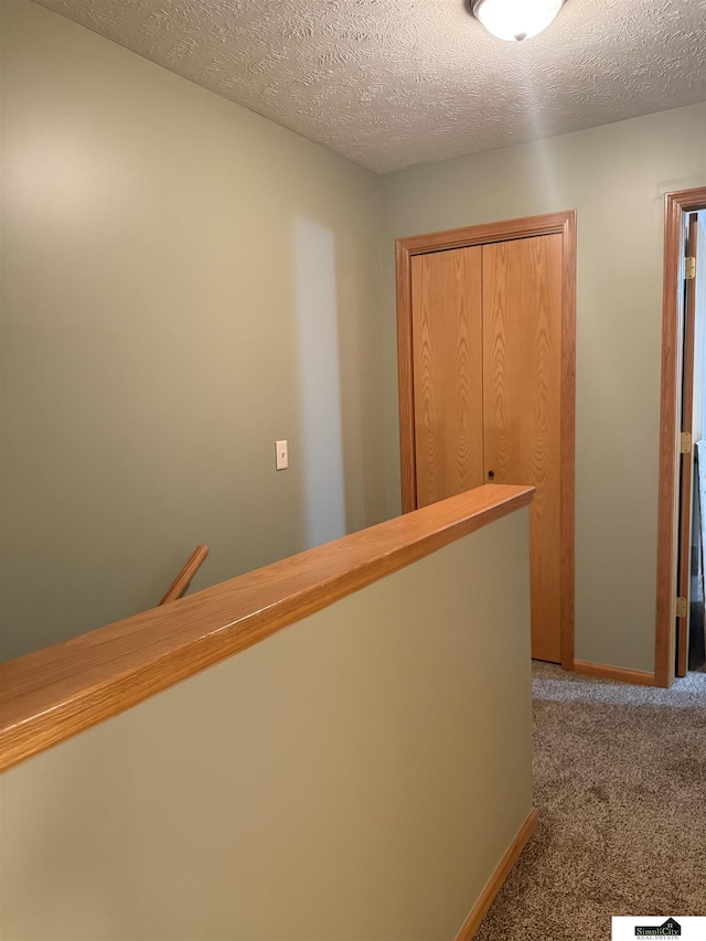 hallway featuring baseboards, carpet floors, and a textured ceiling