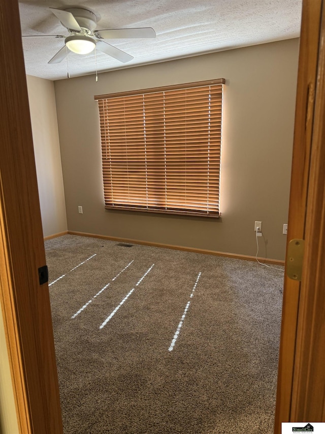 carpeted empty room with baseboards, visible vents, a textured ceiling, and a ceiling fan