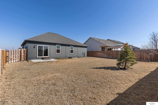 back of property with a lawn, roof with shingles, a fenced backyard, and a patio area