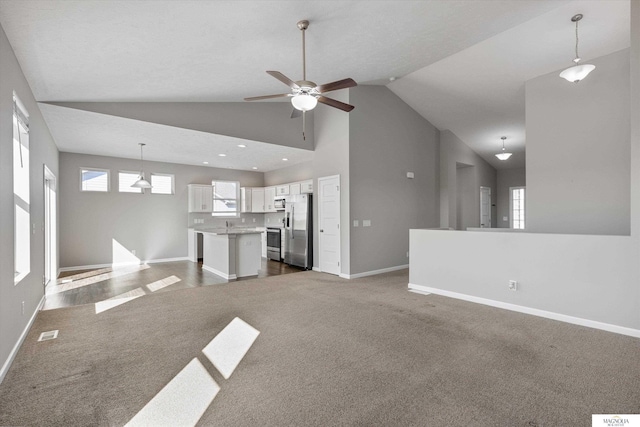 unfurnished living room with high vaulted ceiling, plenty of natural light, baseboards, and ceiling fan