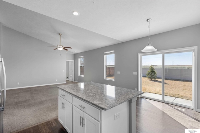 kitchen with dark wood-type flooring, light stone counters, a center island, white cabinetry, and ceiling fan