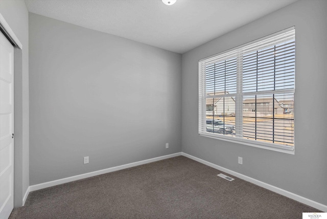 unfurnished room featuring visible vents, baseboards, and dark carpet