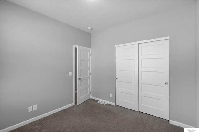 unfurnished bedroom featuring visible vents, baseboards, a closet, a textured ceiling, and dark colored carpet