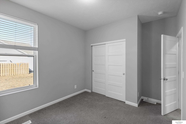 unfurnished bedroom with a closet, multiple windows, baseboards, and dark carpet