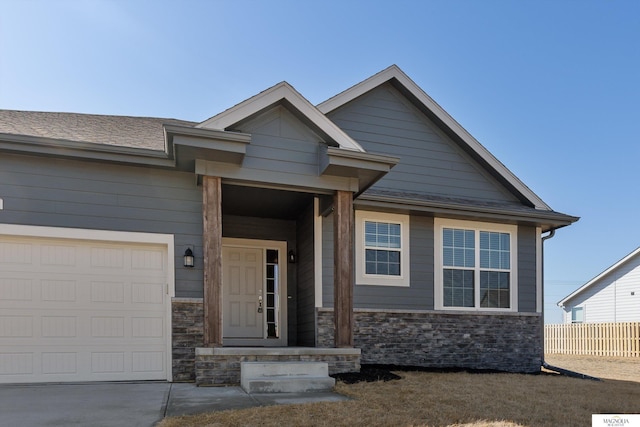 view of front of house featuring stone siding, driveway, a garage, and fence