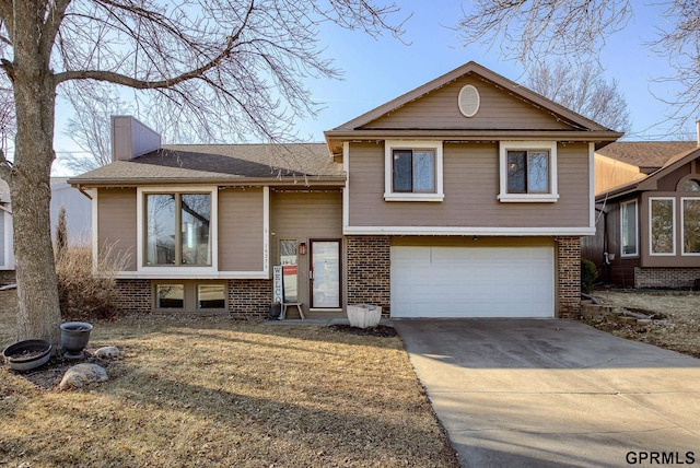 split level home with brick siding, a shingled roof, a chimney, driveway, and an attached garage