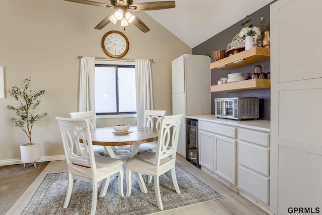 dining room with lofted ceiling, a ceiling fan, wine cooler, light wood-style floors, and baseboards