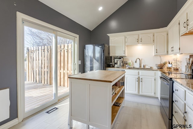 kitchen with visible vents, freestanding refrigerator, stainless steel range with electric cooktop, a sink, and white cabinetry